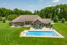 Aerial view of a large suburban home with a swimming pool and well-maintained lawn on a sunny day.