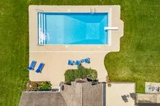 Aerial view of a backyard with a rectangular swimming pool, sun loungers, and a neatly trimmed lawn.