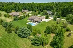 Aerial view of a spacious residential property with a large house, swimming pool, and green surroundings.