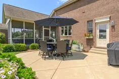 Patio area with outdoor furniture including a table with chairs and an umbrella, adjacent to a brick house, with a clear sky above.