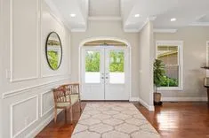 Bright and welcoming entryway with white double doors, a wooden bench, and a decorative mirror on a wall with wainscoting.