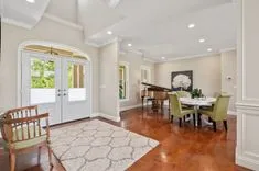 Elegant interior of a spacious home with a grand piano, dining table, and open French doors leading to the outside.
