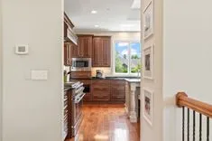 View from a hallway into a modern kitchen with wooden cabinets, stainless steel appliances, and hardwood flooring.