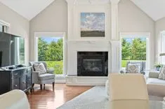 Bright and airy living room with vaulted ceilings, a fireplace, and large windows with a garden view.