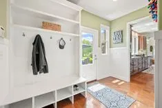 Bright hallway with built-in white storage bench, coat hooks, and open doorway leading to adjacent room.