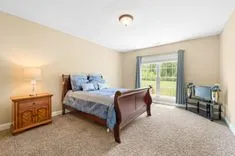 Well-lit spacious bedroom with a queen-sized bed, wooden furniture, and a large window overlooking greenery.
