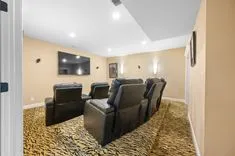Home theater room with tiered leather reclining seats on animal print carpet, large TV on wall, and wall sconces for lighting.