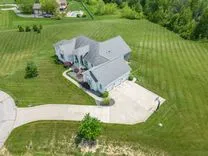 Aerial view of a large detached house with a well-maintained lawn, driveway, and outdoor pool on a sunny day.