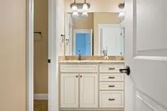 A modern bathroom vanity with granite countertop and white cabinets viewed through an open door.