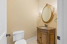 Elegant small bathroom with ornate vanity and mirror, sconce lighting, white toilet, and tiled floor.