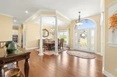Elegant interior of a spacious home with hardwood floors, decorative columns, an ornate mirror, a dining table set, and double doors with frosted glass design letting in natural light.