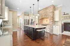 Spacious modern kitchen with a large stone archway over the stove, granite countertops, hardwood floors, and pendant lighting.