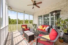 Bright and cozy screened porch with red cushioned furniture, a colorful rug, and a wooded view.