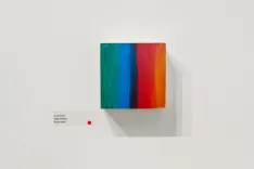 Modern art canvas with vibrant vertical stripes in red, blue, and green, displayed on a white gallery wall with description plaque.