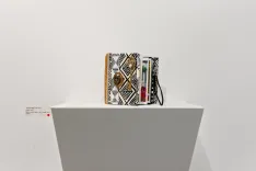 Decorative book clutch bag on a white pedestal in an art exhibit.