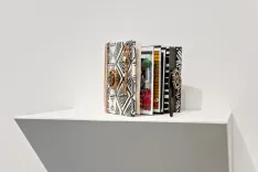 A collection of books with ornate covers displayed on a white shelf against a plain background.