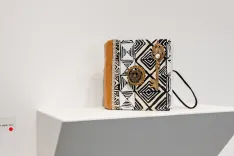 Decorative book with black and white geometric pattern and sun-like motifs displayed on a white shelf with glasses placed beside it.