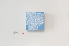 Blue square canvas with intricate white floral patterns on a light wall, accompanied by an information tag on the left and a red security sensor below.