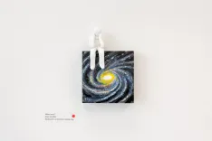 A minimalist art piece featuring a 3D figure seated on top of a canvas painted with a swirling galaxy, hanging on a white wall.