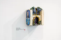 Art installation on a gallery wall featuring a miniature shrine with religious iconography.