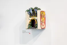 Art installation featuring a colorful diorama with a tunnel-like structure and a tarot card displayed on a white gallery wall.