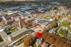 Aerial view of a town with a mix of residential and commercial buildings in autumn, marked with a red location pin.