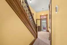 Interior hallway with yellow walls, a wooden stair banister to the left, and a view of a front door with stained glass transom window above.