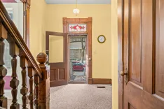 Interior view of a house entryway with decorative stained glass above an open front door, a staircase on the left, and vintage woodwork.