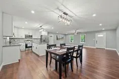 Spacious modern kitchen and dining area with white cabinetry, stainless steel appliances, hardwood floors, and a stylish chandelier over a dining table set.