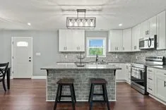 Modern kitchen interior with white cabinetry, stainless steel appliances, subway tile backsplash, granite countertops, and a kitchen island with two stools.
