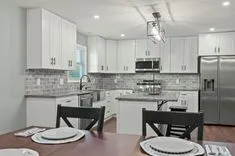 Modern kitchen interior with white cabinetry, stainless steel appliances, and a dining table set for two.