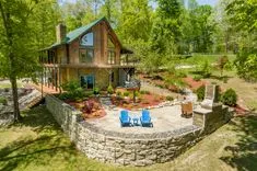 Aerial view of a two-story cabin with a patio and outdoor seating surrounded by lush greenery in a woodland setting.