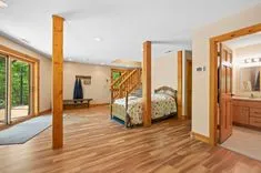 Bright and airy bedroom with hardwood floors, wooden furniture, large windows, and doorway leading to an en-suite bathroom.