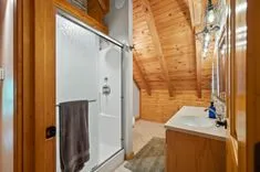 A cozy wooden bathroom interior with a glass shower door, a white sink, and a towel hanging on the wall.