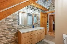 Modern bathroom with stone wall accents, wooden cabinets, and slanted ceiling.