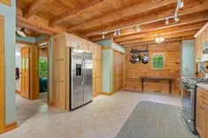 Wooden cabin interior with an open kitchen featuring stainless steel appliances and a dining area with a bench under a wall-mounted bicycle.