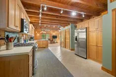 Interior of a spacious kitchen with wooden cabinetry and exposed ceiling beams, featuring modern appliances and a long hallway.
