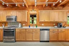 Rustic kitchen interior with wooden cabinets and appliances, including a stainless steel dishwasher and black stove.