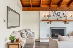 Cozy living room interior with a fireplace, wooden ceiling beams, and decorative 'LAKE' sign above mantel.