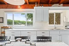 Modern kitchen interior with white cabinetry, stainless steel appliances, and a large window with a view of greenery.