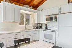 Bright modern kitchen with white cabinets, stainless steel appliances, and wooden ceiling.