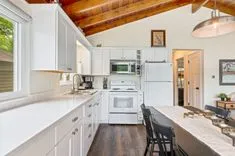 Bright kitchen interior with white cabinetry, stainless steel appliances, and wooden ceiling beams.
