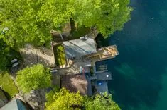 Aerial view of a lakeside house with a dock surrounded by lush trees.