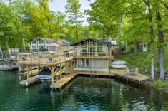 Lakeside house with multiple decks and a boat dock surrounded by lush greenery.