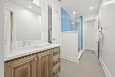 Modern bathroom interior with dual sink vanity, large mirror, and blue tile shower area.