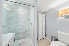 Modern bathroom with glass-enclosed shower, white marble tiles, and a white freestanding cabinet.