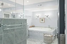 Elegant bathroom interior with a corner bathtub, marble walls, a glass shower partition, wall-mounted towel racks, and decorative lighting fixtures.