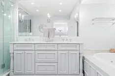 Modern bathroom interior with marble countertop, double sink, large mirror, and a built-in bathtub.