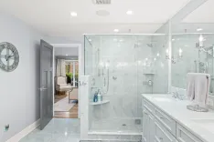 Modern bathroom interior with glass shower, double sink vanity, large mirror, and view into the bedroom.