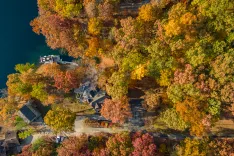 Aerial view of a lakeside landscape during autumn with colorful trees and buildings surrounded by fallen leaves.
